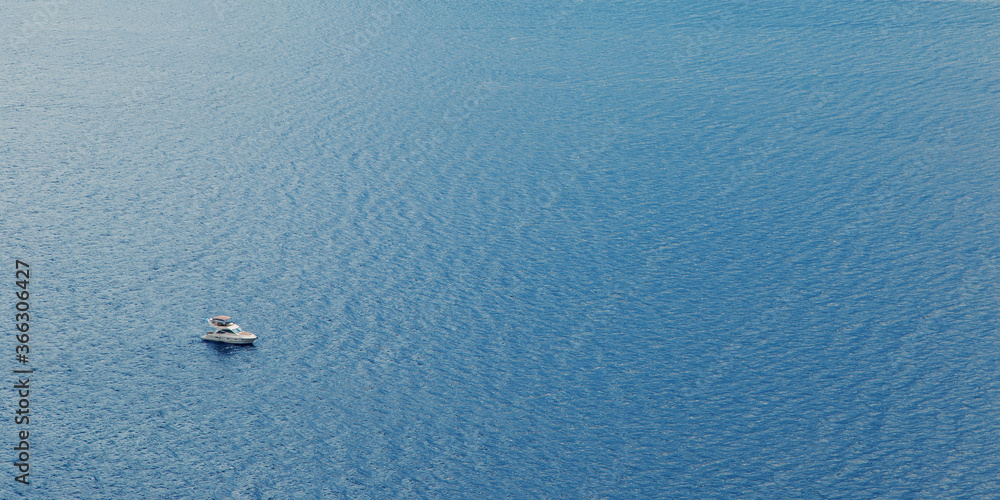 A yacht or a boat floats alone on the big water in sun glare. Open sea without wind. A yacht or a boat floats alone on the big water in sun glare. Open sea without wind.