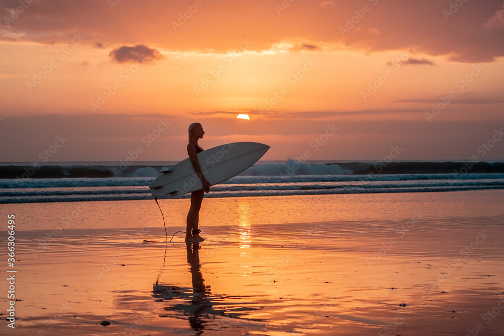 Portrait of surfer girl with beautiful body on the beach with surfboard at colourful sunset time.