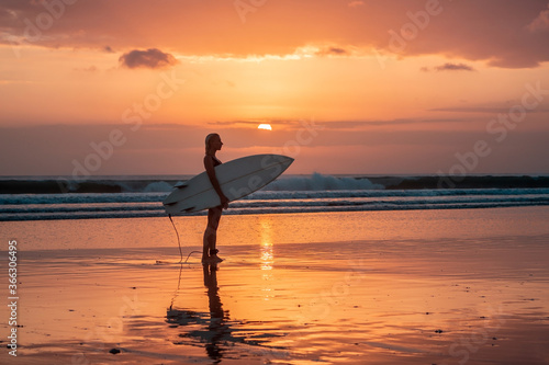 Portrait of surfer girl with beautiful body on the beach with surfboard at colourful sunset time.