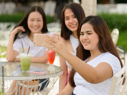 Three happy young Asian women as friends taking selfie together at the coffee shop outdoors