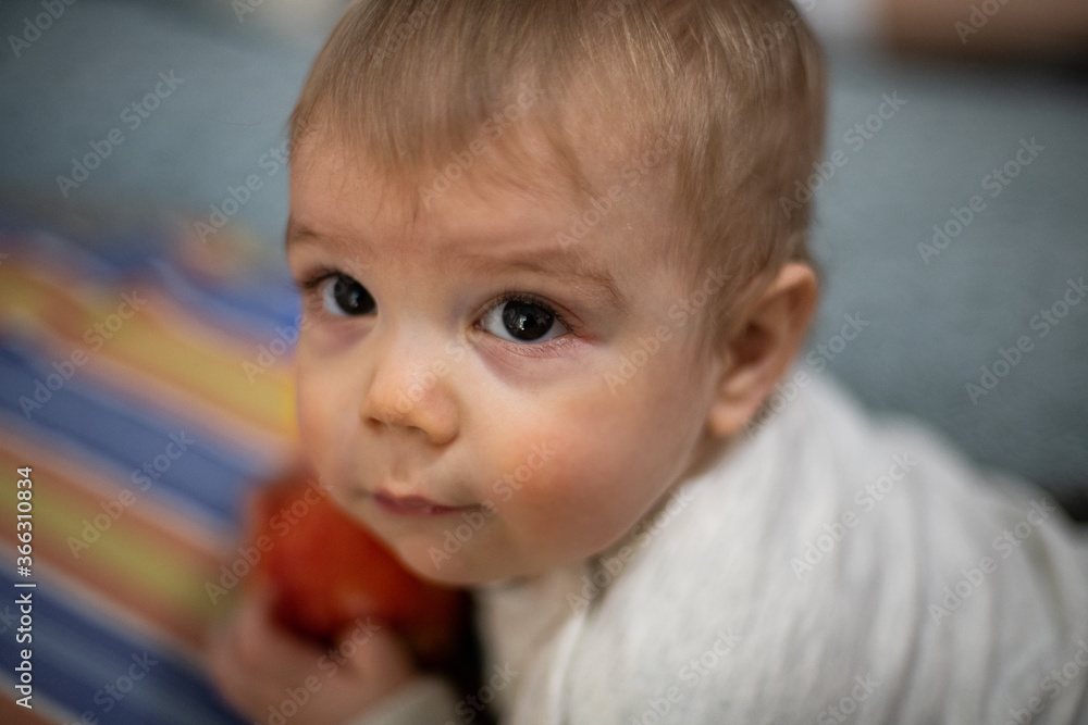 Bebé jugando y comiendo una manzana mirando hacia la cámara