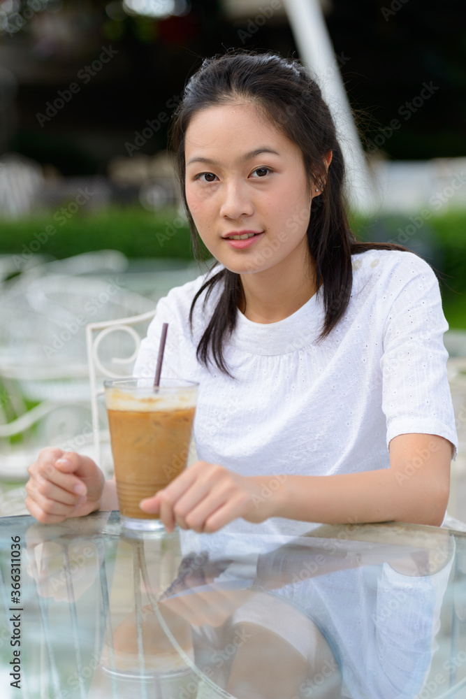 Young beautiful Asian woman sitting at the coffee shop outdoors Young beautiful Asian woman sitting at the coffee shop outdoors