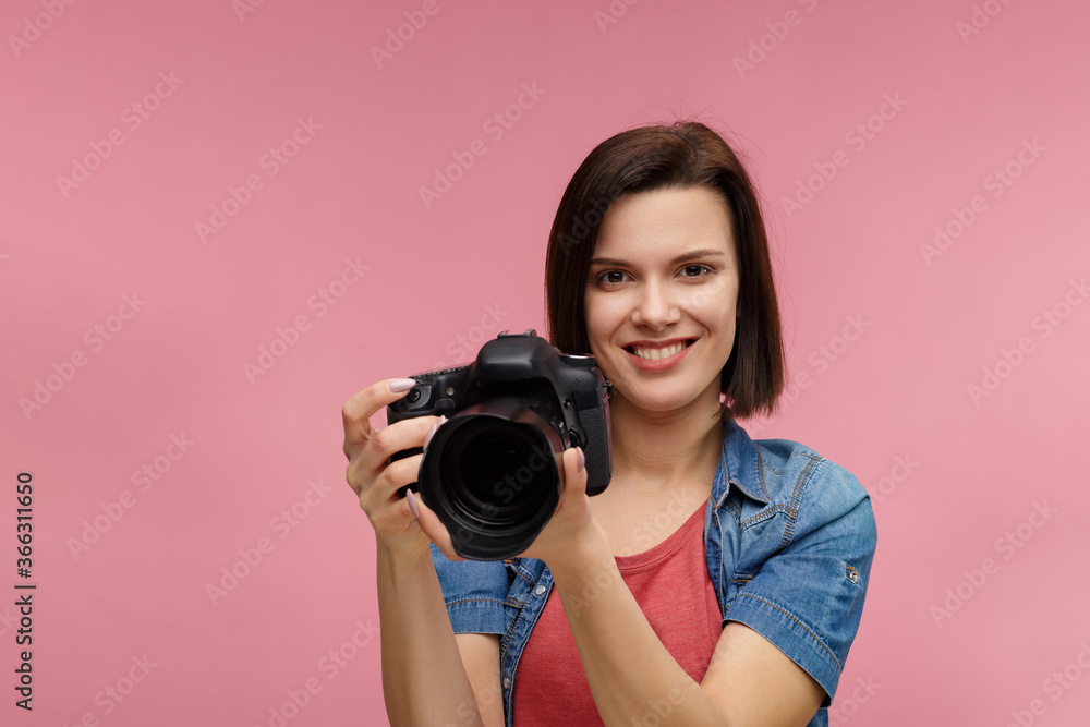 Portrait of young female photographer isolated on pink background with copy space. Photographer with professional camera taking photo in photo studio. Profession, occupation, self-employment. Portrait of young female photographer isolated on pink background with copy space. Photographer with professional camera taking photo in photo studio. Profession, occupation, self-employment.