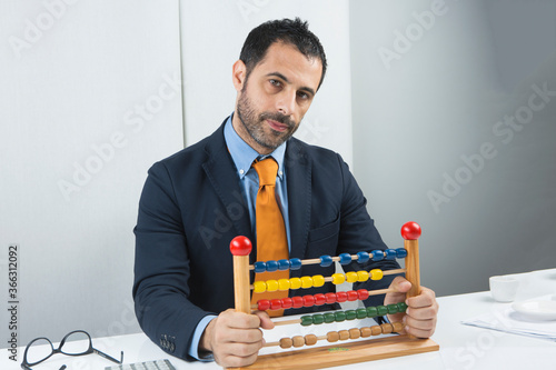 Manager vestito in giacca cca e cravatta nera è seduto nella sua postazione di lavoro mentre fa i conti con un pallottoliere colorato da bambino photo