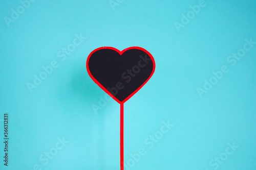 Wooden heart on mint background. Valentines background. Black heart shape on stick over mint background