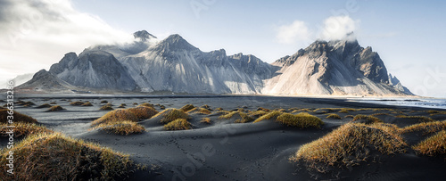 Sunny landscape of Iceland. Gorgeous view on Stokksnes cape and Vestrahorn Mountain with black sand with grass on foreground at summer. Iconic location for landscape photographers. Wonderful nature. photo