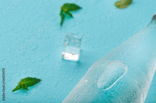 Bottle with an ice cold beverage, ice cubes, drops and mint leaves on a blue background.