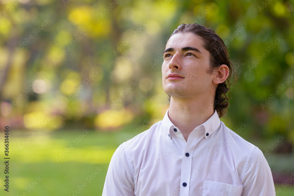 Face of young handsome businessman thinking and looking up at the park outdoors Face of young handsome businessman thinking and looking up at the park outdoors