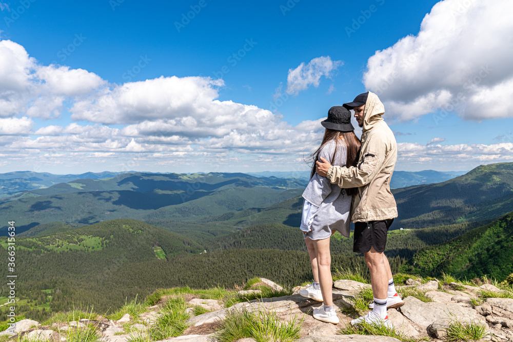Rear view of hikers couple standing on top of the mountain and enjoying the view during the day