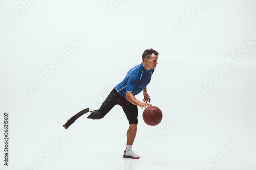 Athlete with disabilities or amputee on white studio background. Professional male basketball player with leg prosthesis training in studio. Disabled sport and healthy lifestyle concept. Achievements.