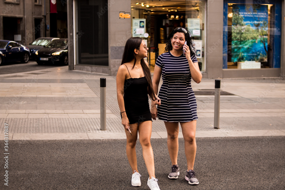 Young women walking around a square in the city while using their electronic devices Young women walking around a square in the city while using their electronic devices