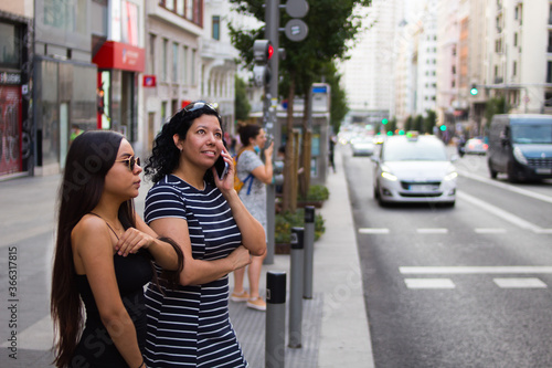 Young women walking around a square in the city while using their electronic devices © Carlos