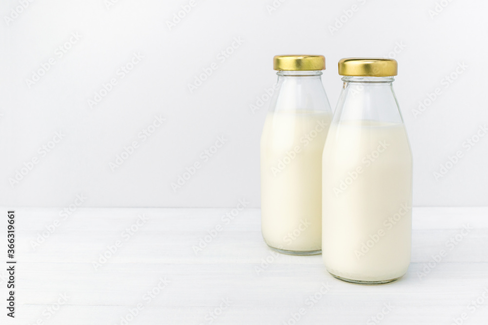 Two bottles of a fresh milk in a glass bottle with golden cap, oatmeal, almond, alternative natural drink. Healthy organic beverage close-up on a white table and light background, copy space. Two bottles of a fresh milk in a glass bottle with golden cap, oatmeal, almond, alternative natural drink. Healthy organic beverage close-up on a white table and light background, copy space.