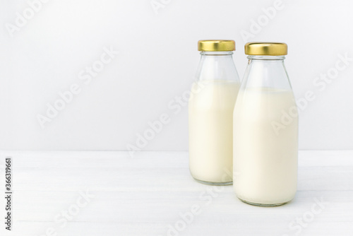 Two bottles of a fresh milk in a glass bottle with golden cap  oatmeal  almond  alternative natural drink. Healthy organic beverage close-up on a white table and light background  copy space.
