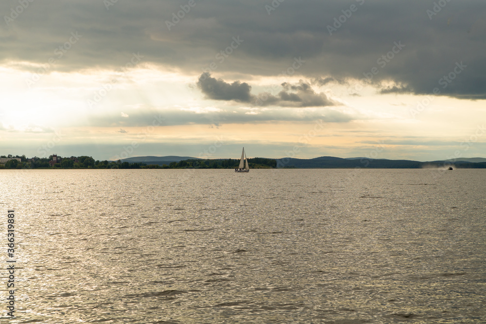 A sailboat floats in a city pond, view from afar from the shore