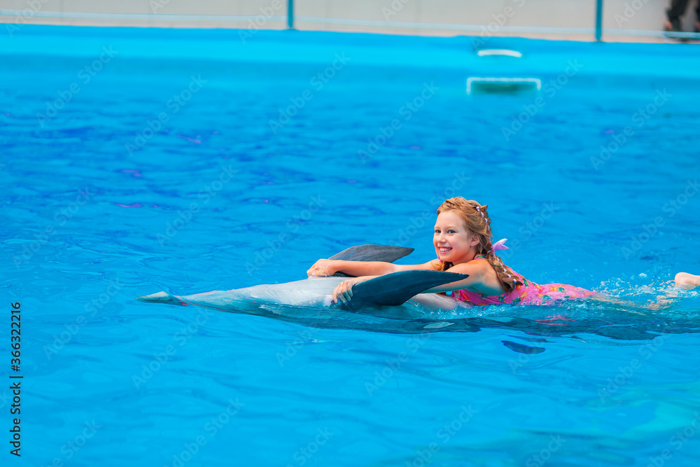 Happy little girl swimming with dolphins in Dolphinarium