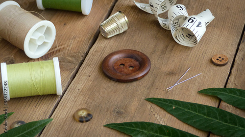 Rustic Sewing Equipment | Wooden Button with Thimble, Sewing Needles and Spools of Thread on a Wood Surface