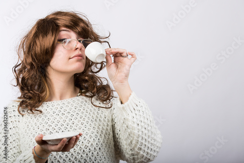 Tableau sur toile Signora con capelli mossi castani e maglione bianco beve il suo caffe da una taz