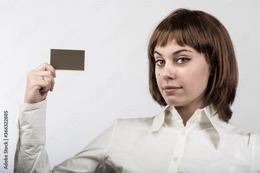 ragazza con capelli a caschetto castani , e camicia bianca mostra una carta tenuta in sospeso sulla mano destra, isolata su sfondo bianco ragazza con capelli a caschetto castani , e camicia bianca mostra una carta tenuta in sospeso sulla mano destra, isolata su sfondo bianco