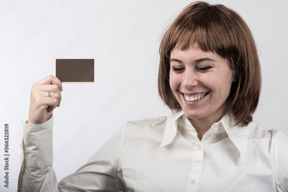 ragazza con capelli a caschetto castani , e camicia bianca mostra una carta tenuta in sospeso sulla mano destra, isolata su sfondo bianco ragazza con capelli a caschetto castani , e camicia bianca mostra una carta tenuta in sospeso sulla mano destra, isolata su sfondo bianco