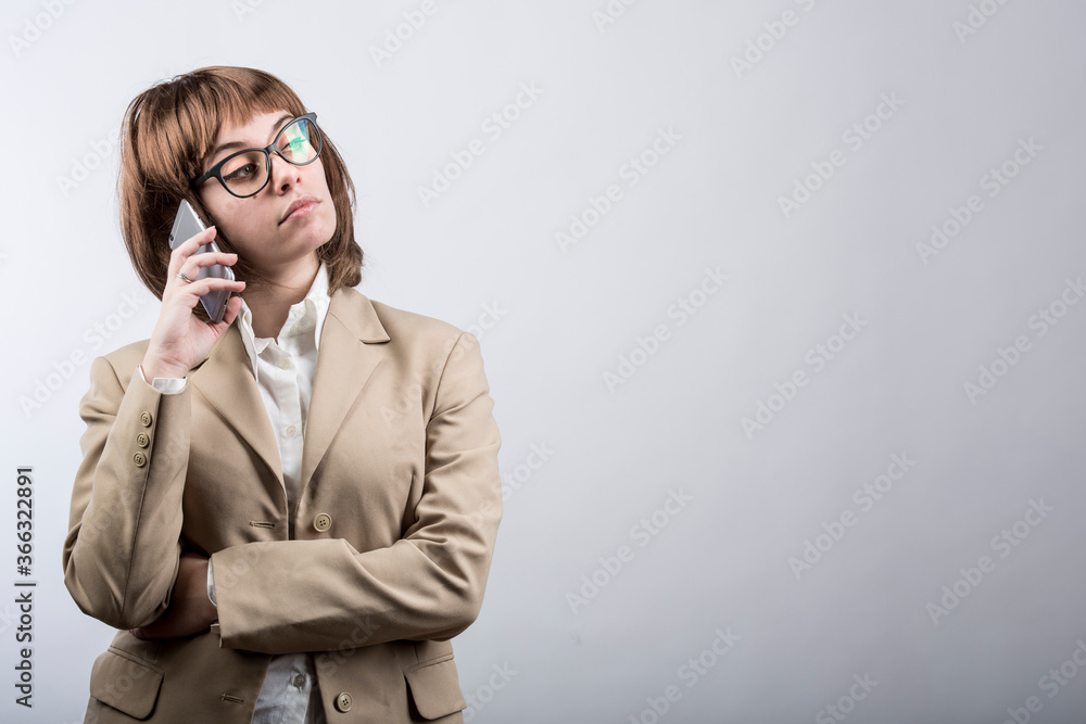 ragazza con capelli a caschetto castani , occhiali e giacca beige utilizza il suo smartphone per mettersi in contatto con un altra persona, isolata su sfondo bianco ragazza con capelli a caschetto castani , occhiali e giacca beige utilizza il suo smartphone per mettersi in contatto con un altra persona, isolata su sfondo bianco