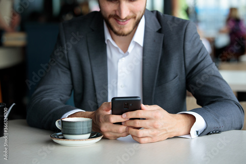 Cropped image of businessman drinking coffee and typing a message in his mobile phone. Businessman typing a message.