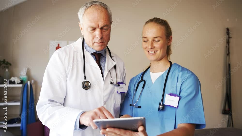 Male doctor in coat and female doctor in scrubs discussing results on digital tablet, happy and smiling Male doctor in coat and female doctor in scrubs discussing results on digital tablet, happy and smiling