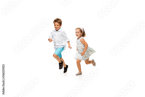 Happy children, little and emotional caucasian boy and girl jumping and running isolated on white background. Look happy, cheerful, sincere. Copyspace for ad. Childhood, education, happiness concept.