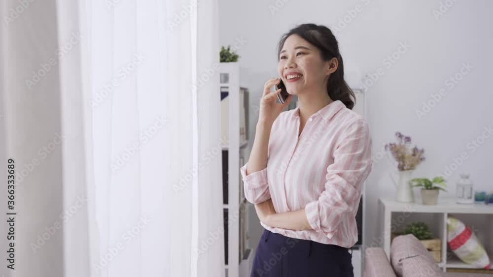 asian woman standing by window getting a phone call from an important shareholder. taiwanese manager explaining plan with hand gesture asian woman standing by window getting a phone call from an important shareholder. taiwanese manager explaining plan with hand gesture