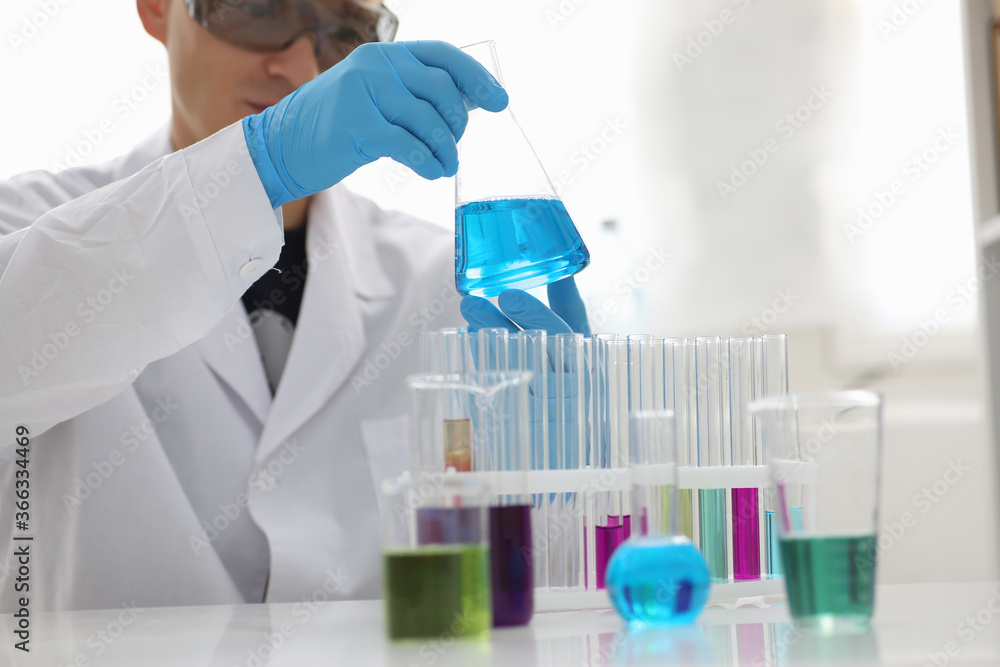 Attentive male person wearing protective uniform while doing chemical experiment in the laboratory Attentive male person wearing protective uniform while doing chemical experiment in the laboratory