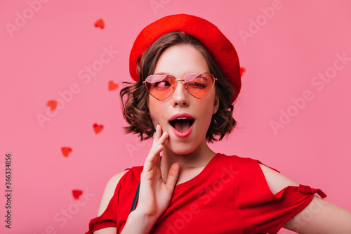 Playful short-haired girl standing on rosy background during romantic photoshoot. Sensual french white woman celebrating valentine's day.