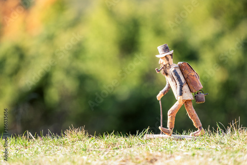 Old wooden carved out man hiker figure, with backpack, walking stick, tobacco pipe and hat outdoors in nature. Blurred out background, copy space for text.