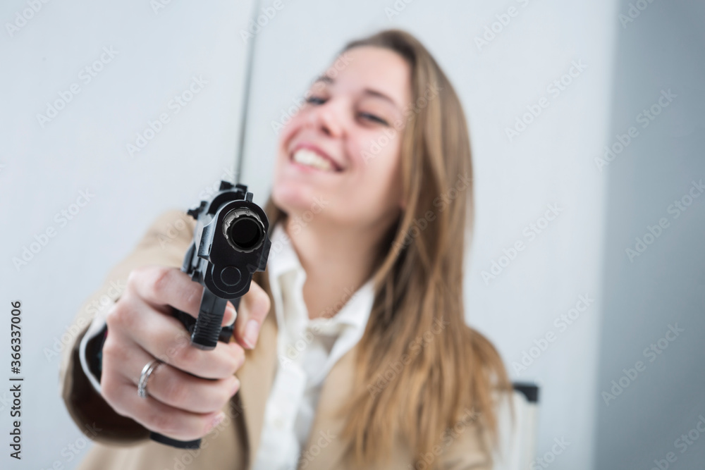 ragazza bionda vestita con una giacca beige è seduta nella sua postazione di lavoro tiene una pistola in mano pronta ad usarla ragazza bionda vestita con una giacca beige è seduta nella sua postazione di lavoro tiene una pistola in mano pronta ad usarla