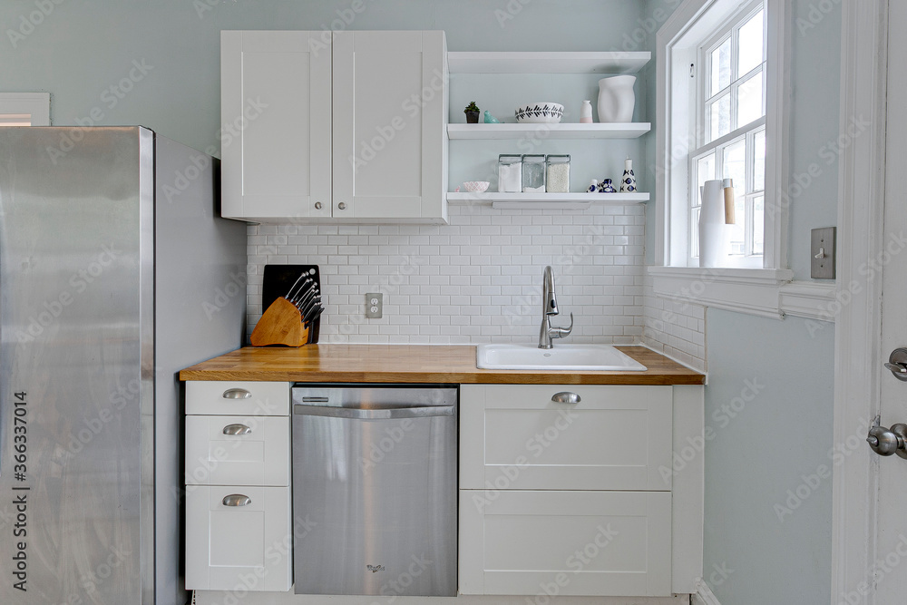 Plain gray kitchen with white subway tile backsplash butcher block countertop white sink modern farmhouse drawers open shelves stainless steel appliances refrigerator and dishwasher Plain gray kitchen with white subway tile backsplash butcher block countertop white sink modern farmhouse drawers open shelves stainless steel appliances refrigerator and dishwasher
