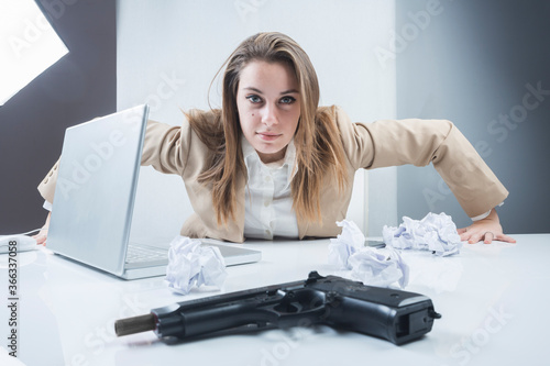 ragazza bionda vestita con una giacca beige è seduta nella sua postazione di lavoro e sbatte le mani sulla scrivania con una pistola in primo piano photo