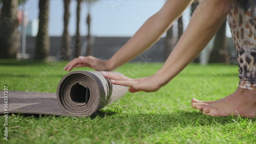 Woman hands rolling up yoga mat after training in park.Girl folding mat on grass