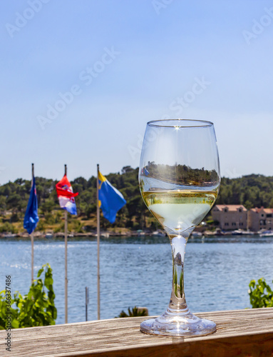 Croatia, Dalmatia, Makarska. A glass of white wine on the counter of an open restaurant with a view of the sea, seaside houses and flags of Croatia. Summer vacation in a Mediterranean resort