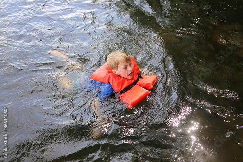 Fototapeta Naklejka Na Ścianę i Meble -  Kid Swimming in Lake Water Looking Distressed and Wearing a Life Vest