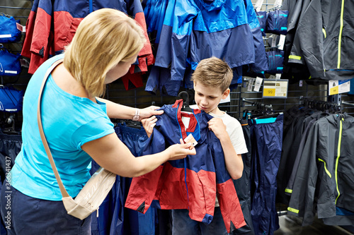 Boy with mom choosing jacket in shop