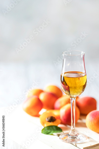 Apricot liqueur in shot glass and fresh apricots on a light wooden table.