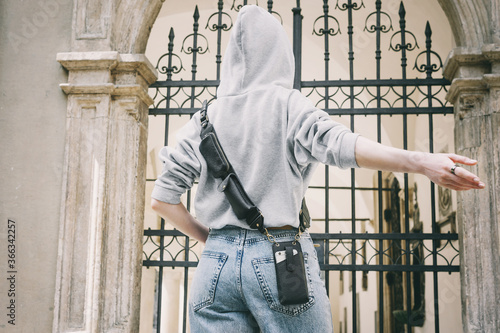 Girl with a strap for a cell phone in a light gray sweatshirt in the hood. Back view. Convenient small bag for walks. Unisex. With this bold leather crossbody belt will hold everything