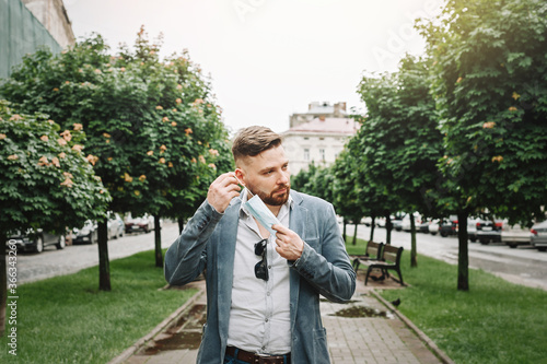 Photography Stylish presentable Caucasian man puts on a disposable medical mask on the street