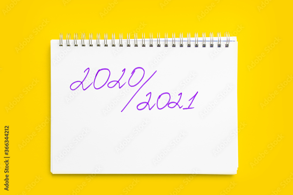 Concept of the new school year and return to school. Inscription 2020 - 2021 in a white notebook with a spiral, on a yellow background. Mockup with place for text.