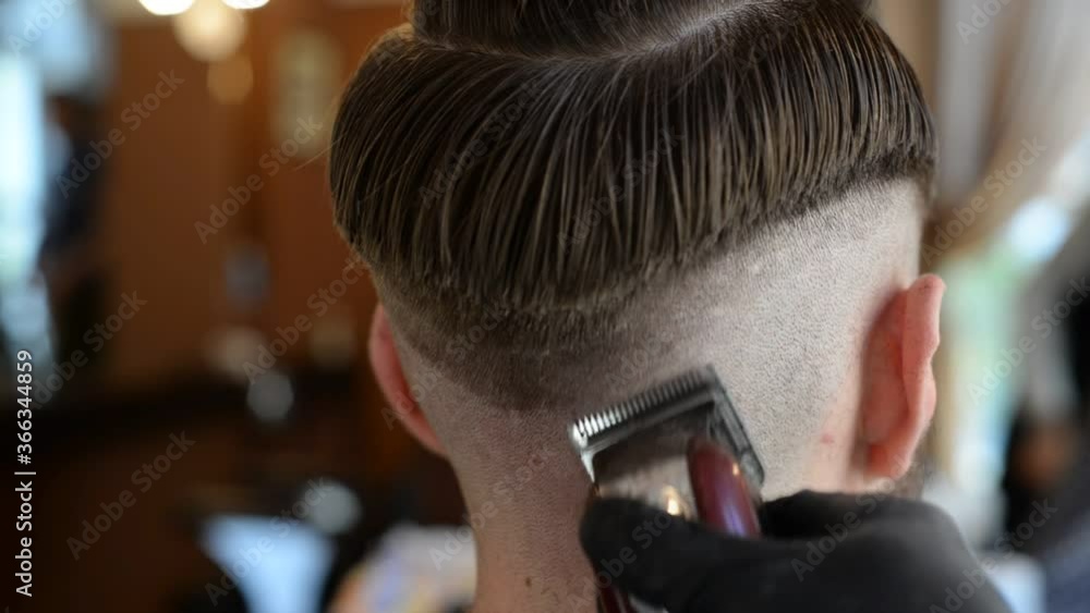 a hairdresser cuts a bearded young guy with a hair trimmer, combing the hair on his head. Work of the master in men's haircut in a barbershop a hairdresser cuts a bearded young guy with a hair trimmer, combing the hair on his head. Work of the master in men's haircut in a barbershop