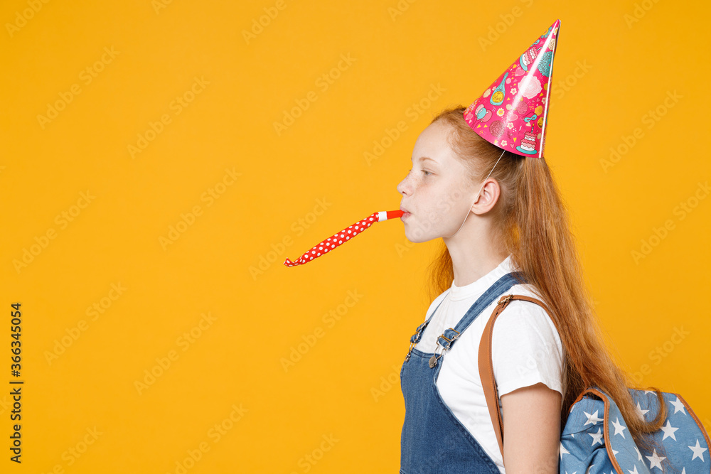 Happy fun redhead school teen kid girl 12-13 years old in birthday hat white t-shirt blue uniform backpack celebrate isolated on yellow background children studio portrait Education lifestyle concept