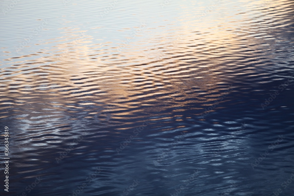 Silver surface of calm water with golden highlights and reflections. Ripples on water surface close-up. Glowing surface of the water. Silver metal surface with golden highlights close-up. Abstract.