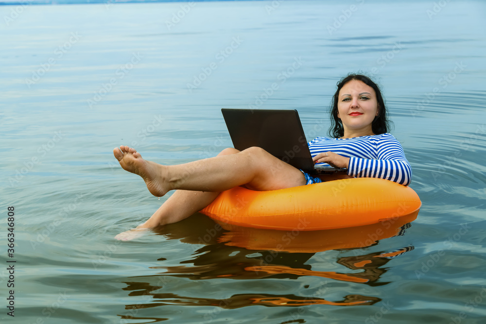 Woman works remotely with laptop in a swimming circle in water.