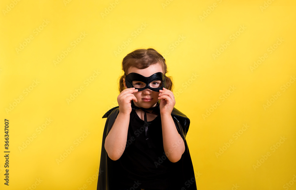 a little girl a superhero in a mask and Cape on a yellow isolated background with space for text a little girl a superhero in a mask and Cape on a yellow isolated background with space for text