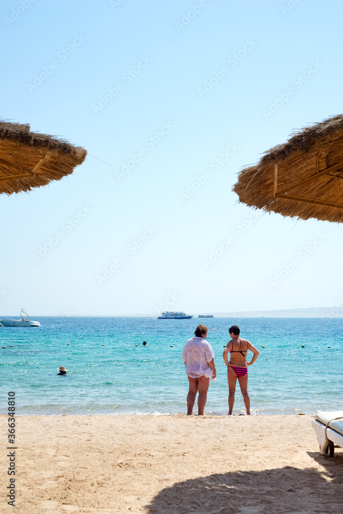 Two women are standing on a beach and talking.