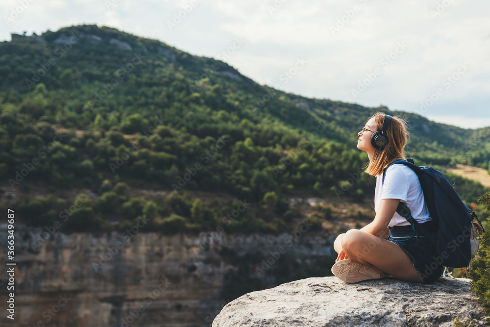  girl meditates on top of mountain, tourist woman with backpack listens music with headphones enjoy hiking background panorama landscape on vacation outdoors empty space
